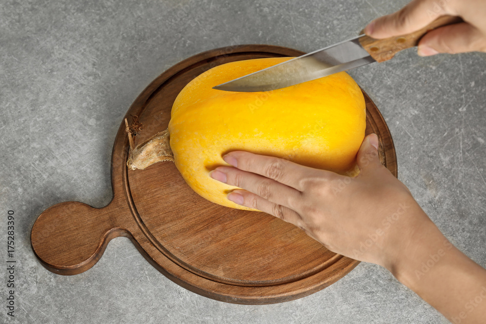 Woman cutting ripe spaghetti squash on wooden board