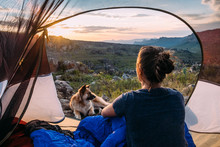 Woman With Her Dog Sitting In Her Tent Watching Sunset
