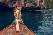 Young Beautiful Blonde Girl Cruising On Retro Wood Boat By Andaman Sea And Behind Her You Can See Ko Phi Phi Lee Island In Full Glory. Dressed In Beautiful Blue Dress And Wearing Straw Hat.
