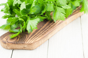 Heap of green fresh raw celery on brown cutting board on old wooden white rustic planks