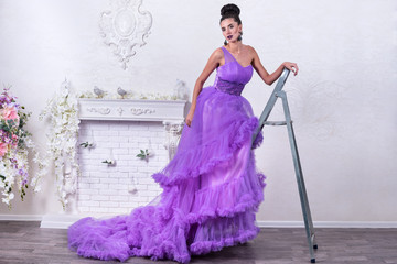 Beautiful woman in a long ball dress on a metal stepladder. Studio portrait