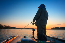 A Fisherman Fishing In A Lake At Sunset