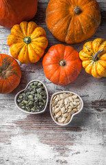 Overhead colorful pumpkins group and seeds in two heart shaped white jars on white rustic table in studio