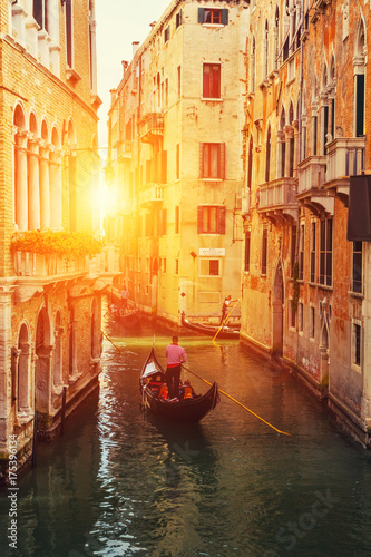 Venetian gondolier punting gondola in water canal with green water