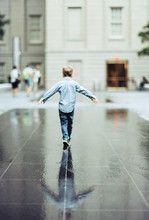 Boy Balancing As He Walks A Straight Line On A Wet Reflective Surface