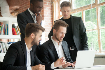 Wall Mural - Multiethnic team of corporate employees looking at laptop screen. Businessman typing on computer screen, african american colleague smiling. Group of coworkers browsing new investment opportunities.