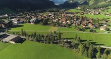 Beautiful Countriside Aerial Shot Of Idyllic Mountain Scenery In The Alps With Traditional Chalets,farm In Alpine Meadows.Green Fields,famous Stunning Touristic Town With High Cliffs In Background.
