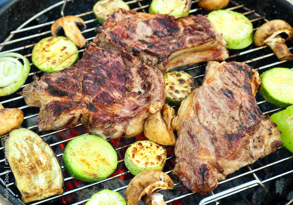 Tasty steaks and vegetables cooking on barbecue grill, closeup