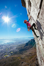 Female Rock Climber Climbing A Sheer Cliff Overlooking A City
