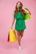 © Drobot Dean - Full length portrait of young charming readhead curly woman with freckles, in green dress, holding colourful shopping bags