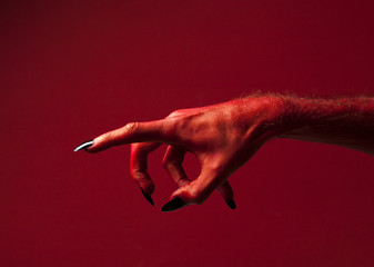 Halloween red devil monster hand with black fingernails against a red background