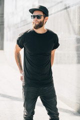 Wall Mural - Hipster handsome male model with beard  wearing black blank  t-shirt with space for your logo or design in casual urban style