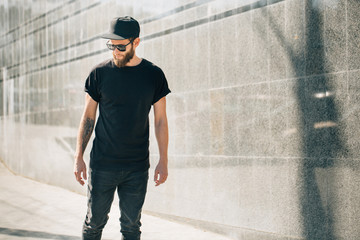 Hipster handsome male model with beard  wearing black blank  t-shirt with space for your logo or design in casual urban style