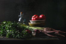 Bowl Of Tomatoes With Purple Carrot, Onion And Bottle Of Olive Oil On Old Wooden Kitchen Table. Dark Rustic Still Life.
