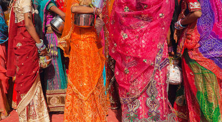 Beautiful crowd of colorfu women dressed traditional indian sari with patterns going for water with jars