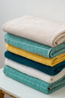 Stack of folded cotton bath towels in beige, turquoise, yellow and teal color on a white table with wooden legs, close-up