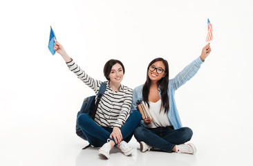 Sticker - Two joyful female students waving us flags while sitting together