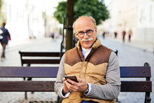 Trendy Mature Guy Using Smartphone On Public Bench Street City