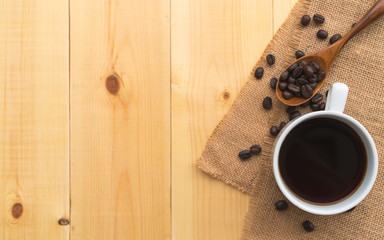 Wall Mural - A cup of coffee and coffee bean grain on sack fabric put on pine wood table background include copyspace for add text or graphic