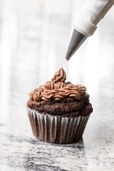 Piping bag with chocolate ganache cream above chocolate cup cake on the grey granite background