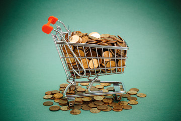 Wall Mural - Shopping trolley with coins on a green background