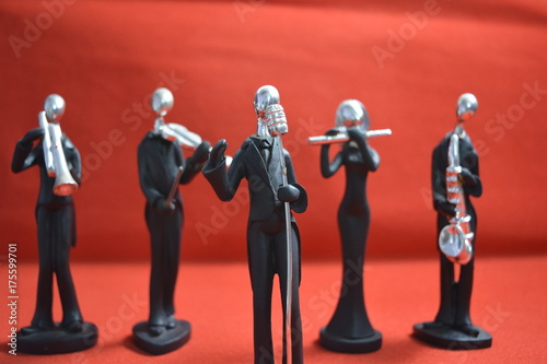 Zdjęcie XXL Zabawkarski mężczyzna z mikrofonem i muzykami na czerwonym tle.