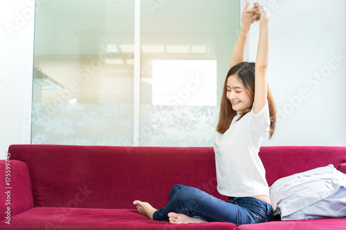 Plakat Młoda azjatykcia piękna kobieta siedzi relaksującego freetime w ranku na czerwonej leżanki kanapy żywym pokoju w domu