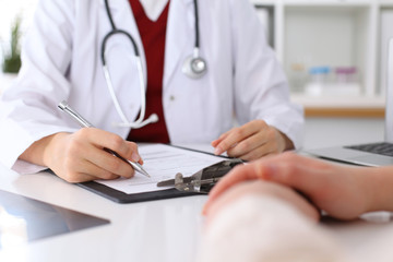 Close up of a female doctor filling up  an application form while consulting patient