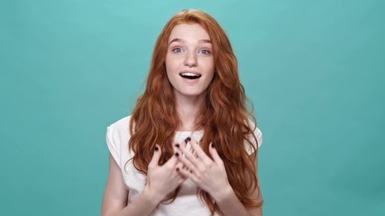 Poster - Happy ginger woman in t-shirt covering her face and rejoice after that while looking at the camera over turquoise background