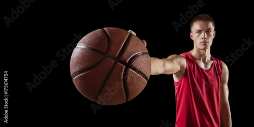 Zdjęcie XXL Gracz koszykówki trzymać piłkę do koszykówki. Odosobniony gracz koszykówki na czarnym tle. Gracz nosi ubrania niemarkowe.