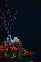 Wall Mural - Tree branches in a glass bottle on a stack of wooden boxes, dark still life with a halloween mood and autumn leaves