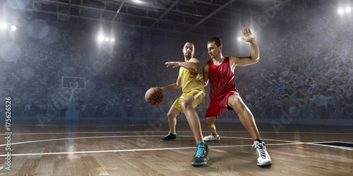 Plakat Dwóch graczy w koszykówkę walczy o piłkę do koszykówki na dużej arenie zawodowej. Gracz nosi ubrania niemarkowe.