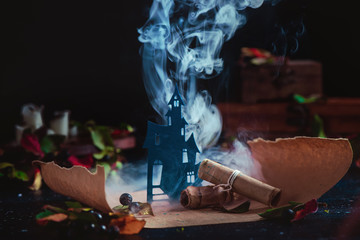 Wall Mural - Haunted castle in clouds of smoke on a magical scroll. Conceptual Halloween still life with smoke, wirards workplace, leaves, candles and spells. Occult scene with copy space.