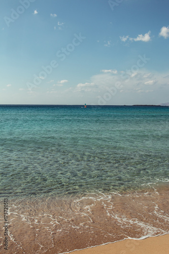 Greek beach with turquoise water and someone doing windsurf in the distance
