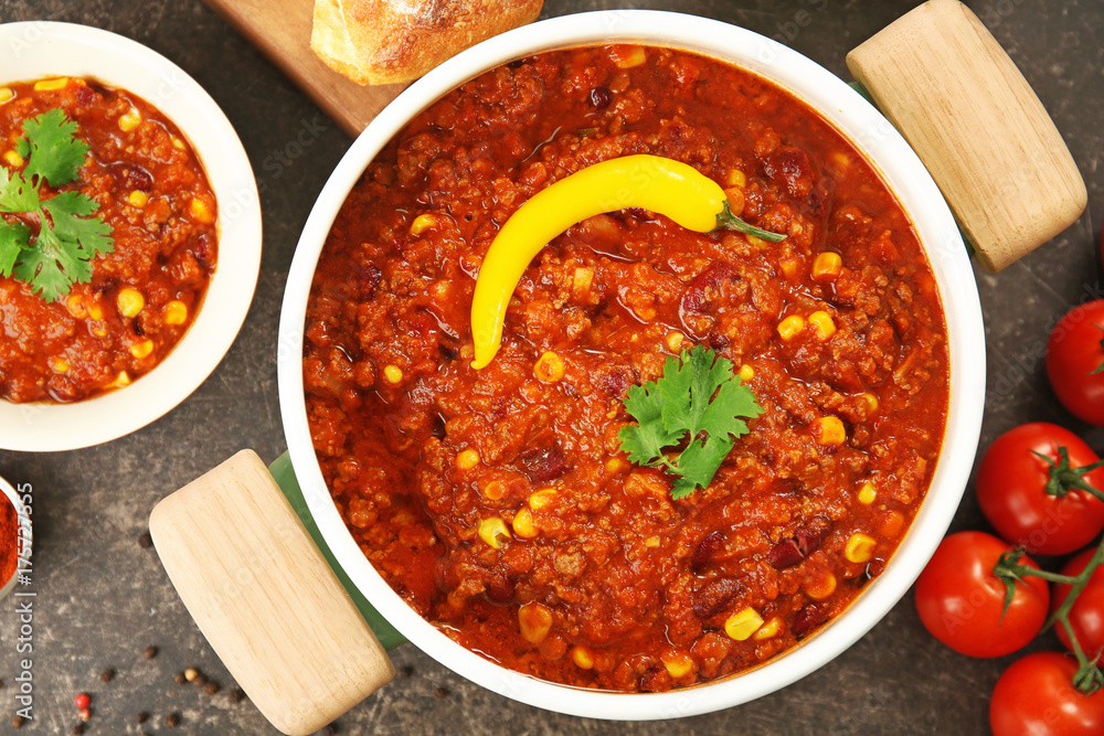 Saucepan and bowl with delicious chili con carne on table