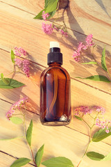 Wall Mural - cosmetic  serum with  extract of flowers. Serum in a brown glass bottle on a wooden background with pink flowers and green leaves. Bio vegan vegetable natural cosmetics concept