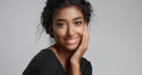 young girl with perfect light brown skin and beautiful curly black hair smiling at the camera in studio