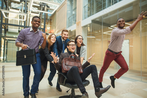 Plakaty do biura positive-colleagues-having-fun-with-office-chairs
