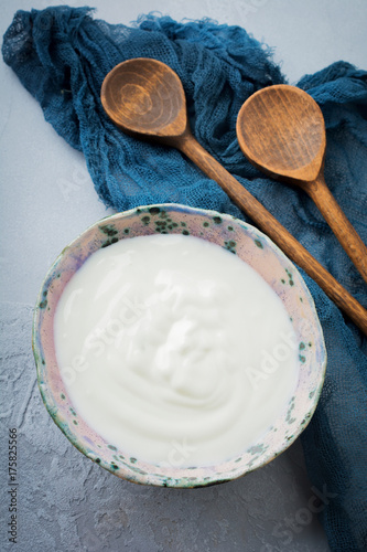 Plakat Grecki jogurt w ceramicznym talerzu z drewnianymi łyżkami na popielatym betonowym tle. Selektywna ostrość. Styl rustykalny.