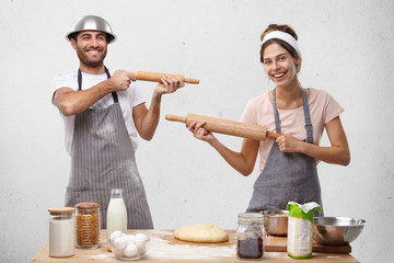 Family couple play fool on kitchen, shoot at each other with rolling pins, rest after making pastry, have good mood and inspiration for work. Real struggle of two talented cooks. Professionalism