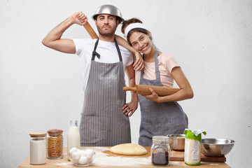 Wall Mural - Isolated pciture of beautiful young Caucasian family male and female feeling happy and proud of themselves as they managed to knead dough together for lasagna or pizza, standing at cooking table