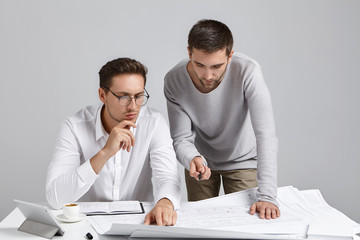 People, collaboration and discussion concept. Professional architect coworkers look attentively at blueprint, develop construction project together, try to omit all drawbacks, make it perfect