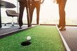© VadimGuzhva - Close up. Men play in an office in a mini golf. One of them holds a golf club in his hands