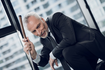 Wall Mural - A respectable elderly man playing a mini golf in the office. He smiles and looks at the miniature golf course