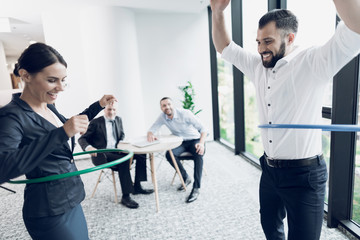 Wall Mural - Fun in the office. A man and a woman twist hula hoops. Two of their colleagues sit at the table and look at them.