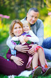© Tortuga - happy family walking in the evening park, sitting on the grass and hugging.