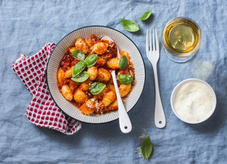 Potato gnocchi in tomato sauce with basil and parmesan and a glass of white wine on blue background, top view. Italian cuisine. Vegetarian food