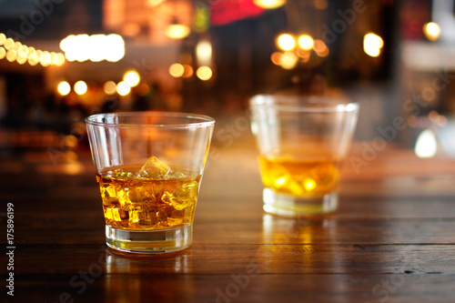 Plakat Whisky szkła piją z kostkami lodu na drewnianym stole w kolorowym noc barze