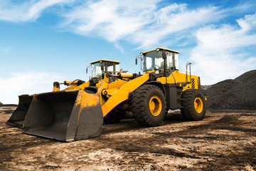 Wall Mural - Old yellow bulldozer with caterpillar moving ground with scoop. Blue sky and white clouds in background