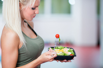 healthy young woman eating salad at gym